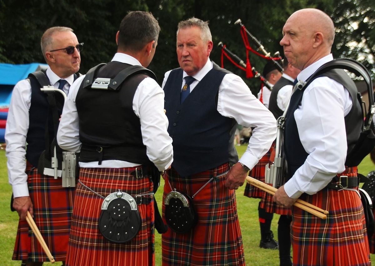 Four band members in kilts talking at the side of a games field